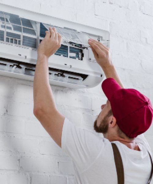 young repairman changing filter for air conditioner hanging on white brick wall