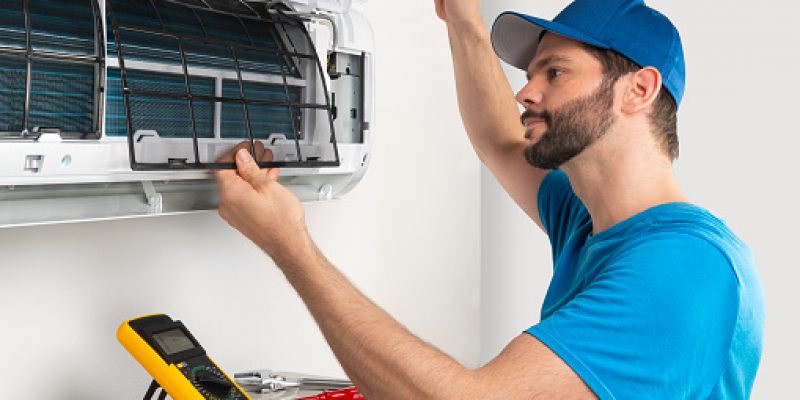 residential-commercial-hvac-repair Installation service fix repair maintenance of an air conditioner indoor unit, by cryogenist technican worker checking the air filter in blue shirt and baseball cap